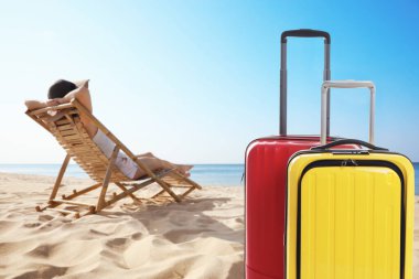 Kumsalda güneşlenen bir kadının yanındaki bavullar. Tatil gezisi