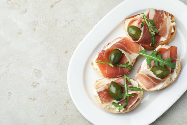 Krem peynirli nefis bruschettalar, prosciutto, yeşil zeytin ve roka, gri desenli masa, üst manzara. Metin için boşluk