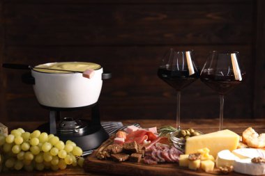 Lezzetli eritilmiş peynirli fondü, ahşap masada atıştırmalıklar ve şarap.