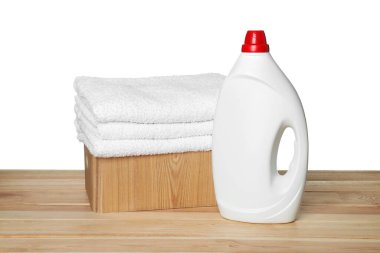 Çamaşır sepeti yumuşak havlular ve ahşap masanın üzerinde beyaz arka planda duran bir şişe deterjan.