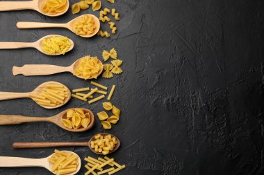 Siyah masadaki tahta kaşıklarda farklı türde çiğ makarna, düz yerde. Metin için boşluk