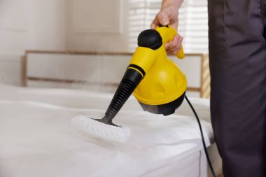 Haşere kontrol işçisi yatağı temizliyor, kapalı alanda buhar temizleyicisiyle, yakın plan