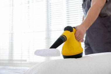 Haşere kontrol işçisi yatağı temizliyor, kapalı alanda buharlı temizleyiciyle, yakın plan. Metin için boşluk