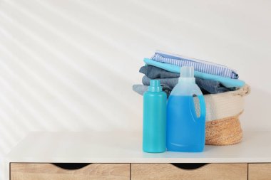 Çamaşır sepetinde giysi ve deterjan var. Beyaz duvarın yanındaki masada. Mesaj için yer var.