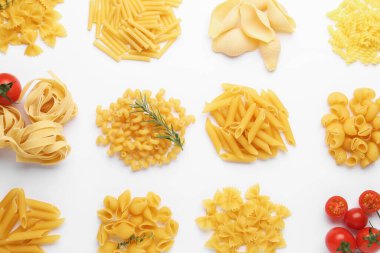 Farklı türde çiğ makarna, domates, biberiye ve kekik beyaz masada, düz yerde.