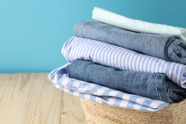 Açık mavi duvarın yanındaki ahşap masada giysileri olan çamaşır sepeti, yakın plan.