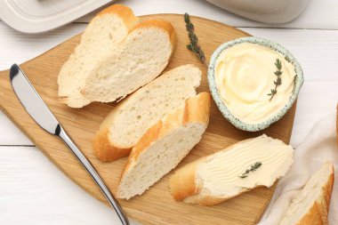 Tereyağlı baget dilimleri, kekik ve bıçak beyaz ahşap masada, düz yatıyordu.