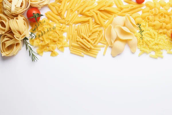 Farklı türde çiğ makarna, domates, biberiye ve kekik, beyaz masa, düz yatak. Metin için boşluk