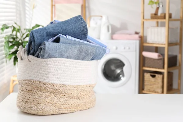Çamaşır sepetinin içinde beyaz masa üzerinde giysiler var. Metin için boşluk