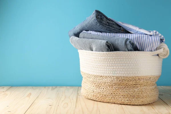 Açık mavi duvarın yanındaki ahşap masada giysileri olan çamaşır sepeti. Metin için boşluk