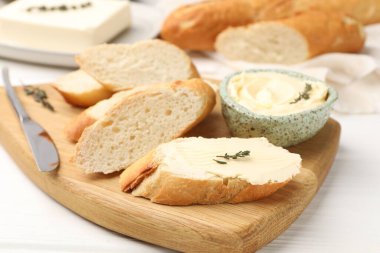 Tereyağlı baget dilimleri, kekik ve bıçak beyaz ahşap masada, yakın plan.