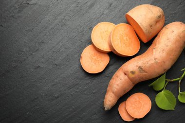 Tüm, tatlı patates ve yeşil yapraklar koyu dokulu masada, düz yerde. Metin için boşluk