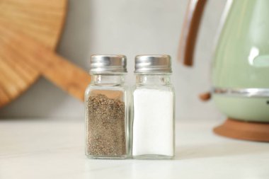 Beyaz masadaki baharatlı tuzluklar ve biberlikler, yakın plan.