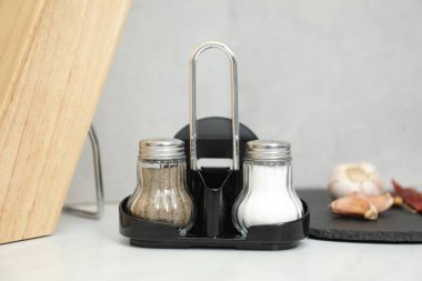 Gri duvarın yanındaki beyaz masada baharatlı tuzluk ve biberlikler, yakın plan.