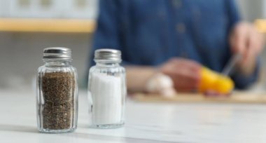 Beyaz mermer masada, tuzluk ve biberlikle evde baharat pişiren bir kadın, seçici bir odak. Metin için boşluk