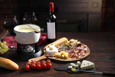 Nefis eritilmiş peynir fondü kabında, abur cuburlar ve bir şişe şarap ahşap masada, karanlık arka planda, yakın planda