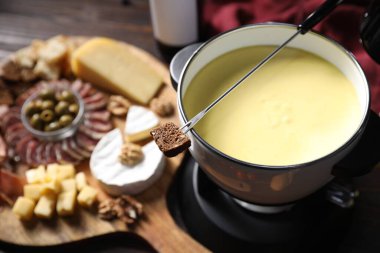 Nefis eritilmiş peynir fondü kabında, çatalla bir parça ekmek ve aperatifler ahşap masada, seçici odaklanma