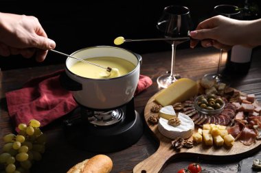 Bir çift ekmek ve üzümü fondü kabına daldırmak ahşap masada lezzetli erimiş peynirle siyah arka planda atıştırmalıklar, yakın plan