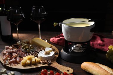 Nefis eritilmiş peynir fondü kabında, abur cuburlar ve bardaklar ahşap masada siyah arka planda, yakın plan