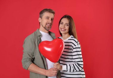 Kırmızı arka planda kalp şeklinde balonları olan mutlu bir çift. Sevgililer Günü kutlaması