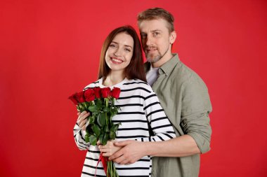 Kırmızı arka planda gül buketi olan mutlu bir çift. Sevgililer Günü kutlaması