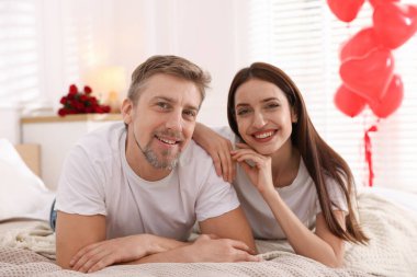 Yataktaki mutlu çift kalp şeklinde balonlarla süslenmiş. Sevgililer Günü kutlaması