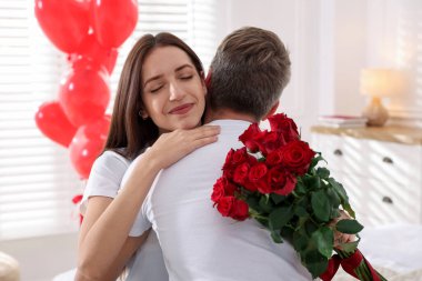 Elinde gül buketi olan bir kadın içeride erkek arkadaşına sarılıyor. Sevgililer Günü kutlaması