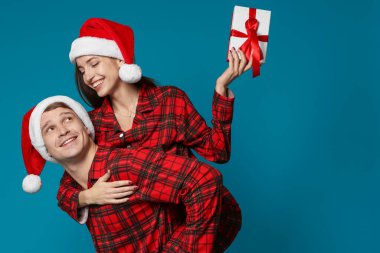 Noel Baba şapkalı ve pijamalı mutlu çift açık mavi arka planda Noel hediyesi