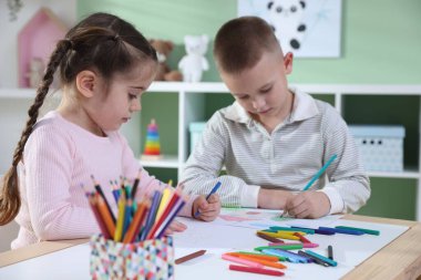 Çocuklar kalem ve pastel boyayla resim çiziyor.