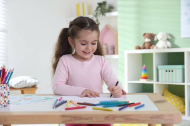 Masada pastel boyayla resim çizen sevimli küçük kız.