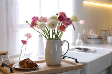 Güzel ranunculus çiçekli ahşap tepsi ve mutfakta taze kruvasan.