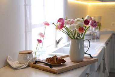 Güzel ranunculus çiçekli ahşap tepsi ve mutfakta taze kruvasan.