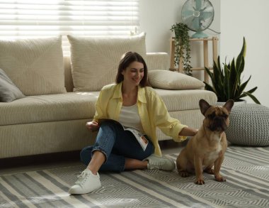 Şirin köpeği ve dergisiyle evdeki kanepenin yanında dinlenen bir kadın.