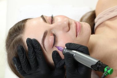 Güzellik uzmanı genç bir kadına kalıcı göz kalemi makyajı yapıyor.