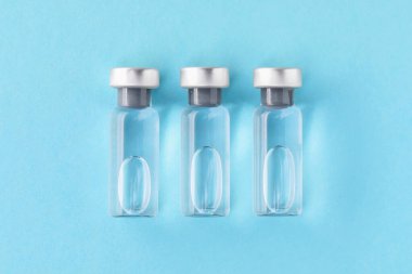 Açık mavi zemin üzerinde cam şişelerde aşı, düz yatıyordu