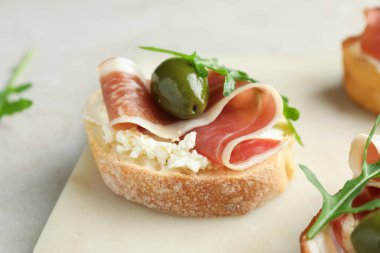 Krem peynirli lezzetli bruschettalar, prosciutto, yeşil zeytin ve roka gri masada, yakın plan.