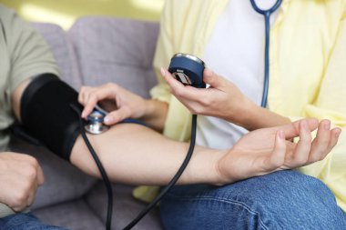 Kadın evdeki kanepede kan basıncını sphygmomanometre ile ölçüyor.