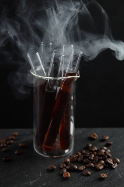 Kahve ve fasulyeli cam test tüpü siyah arka planda dumanlı, yakın plan