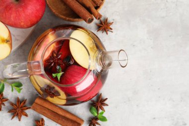 Cam çaydanlıkta aromatik meyve çayı, elmalar, nane ve baharatlar gri masada, düz yerde. Metin için boşluk