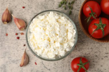 Cam kasede taze süzme peynir, gri masada domates ve baharatlar, düz uzanmış.