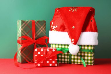 Noel Baba şapkası ve hediye kutuları kırmızı masada yeşil arka planda.