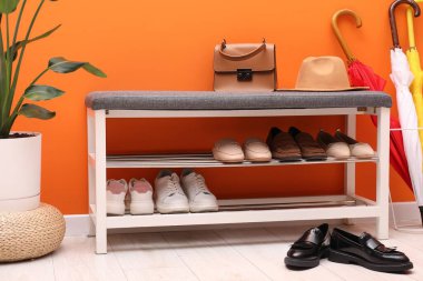 Farklı ayakkabı, aksesuarlar ve turuncu duvarın yanındaki ev bitkileriyle dolu bir ayakkabı deposu.