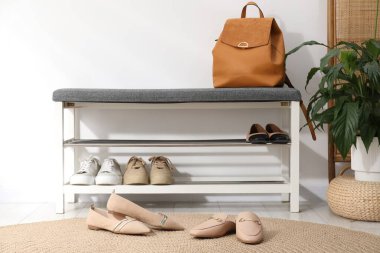 Ayakkabı bankı, farklı ayakkabılar, sırt çantası ve beyaz duvarın yanındaki ev bitkisi.