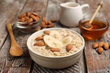 Badem sütlü yulaf ezmesi, fındık, bal ve muz ahşap masada, yakın plan.