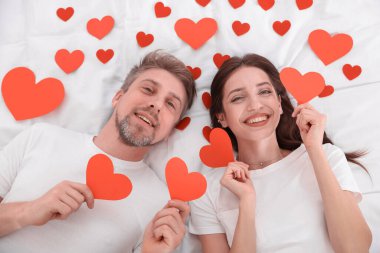 Yatakta kağıt kalpli mutlu bir çift. Sevgililer Günü kutlaması