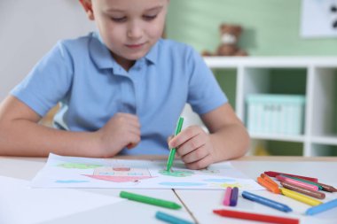 Masada pastel boyayla resim çizen sevimli bir çocuk. Seçici bir odak noktası.