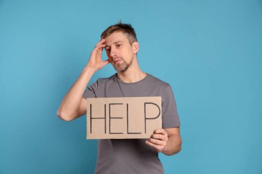 Mutsuz adam elinde kelime yazılı karton tabela açık mavi arka planda yardım