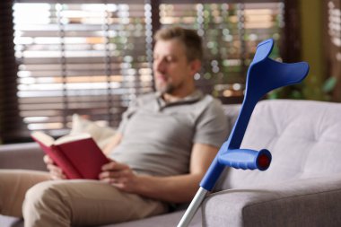 Evdeki koltukta kitap okuyan adam, koltuk değneklerine odaklan.