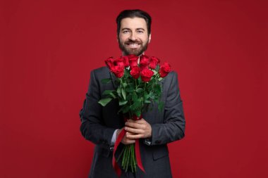 Sevgililer Günü. Kırmızı arka planda gül buketi olan yakışıklı adam.