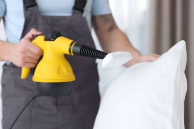 Haşere kontrol görevlisi yastığı temizliyor, kapalı alanda temizliyor, yakın plan.